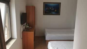 A room with a wooden desk, a television, two beds, and a painting on the wall.