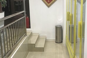 Una escalera con barandilla metálica, un cubo de basura y un ventanal con marco amarillo.