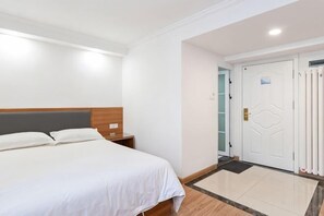 A hotel room with a bed, bedside table, and a door with a handle. - Hongrunde Hotel (Qingdao)