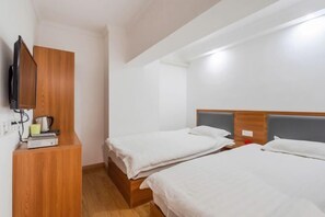 Une chambre d’hôtel avec deux lits, une armoire en bois, une télévision et une petite table avec une bouilloire et des tasses.