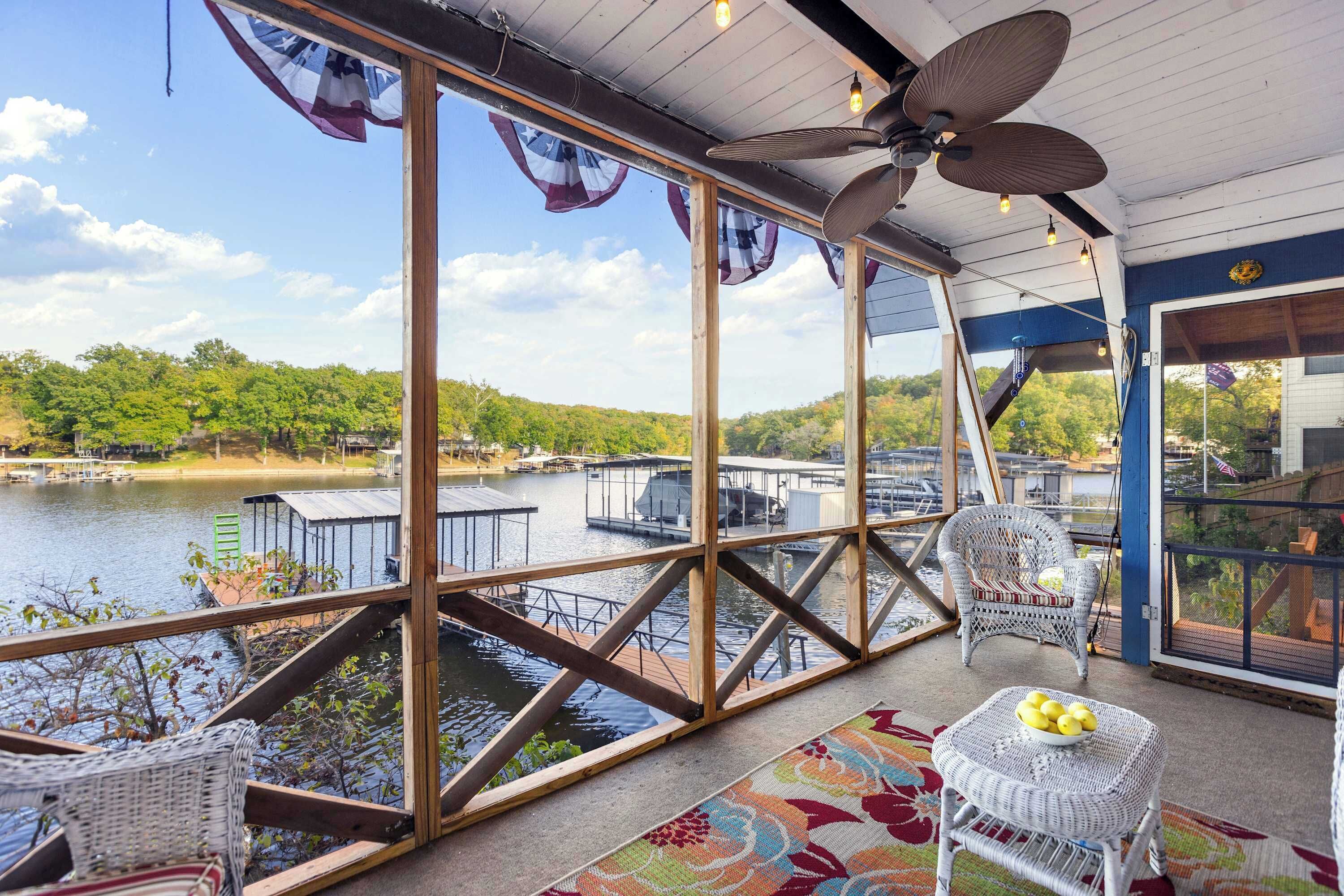 A covered outdoor area with wicker furniture, a fan, and a view of a lake with docks.