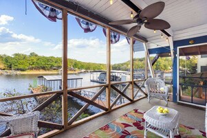 A covered outdoor area with wicker furniture, a fan, and a view of a lake with docks.