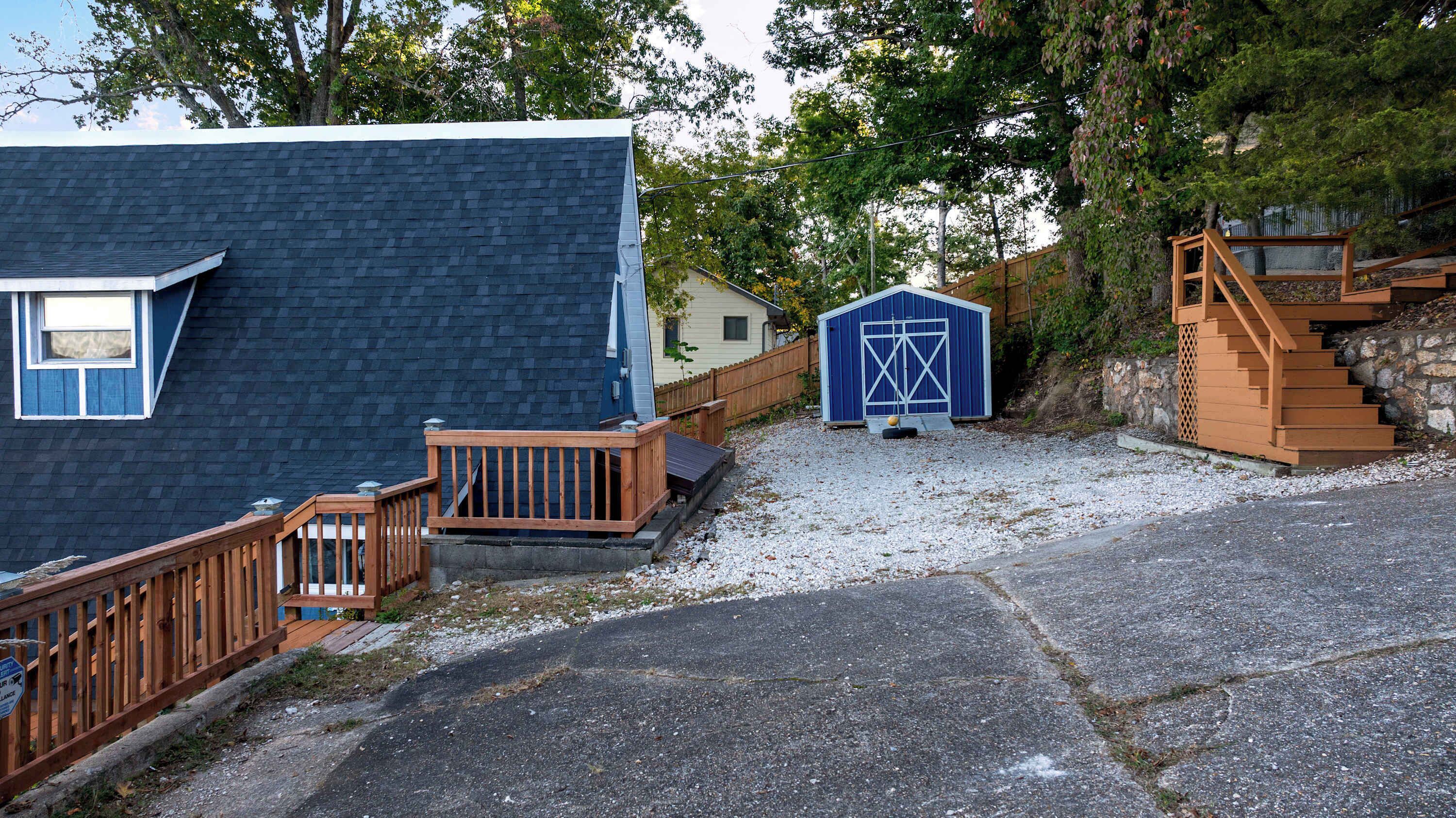 A residential property with a blue house, a wooden deck, a gravel driveway, and a blue garage.