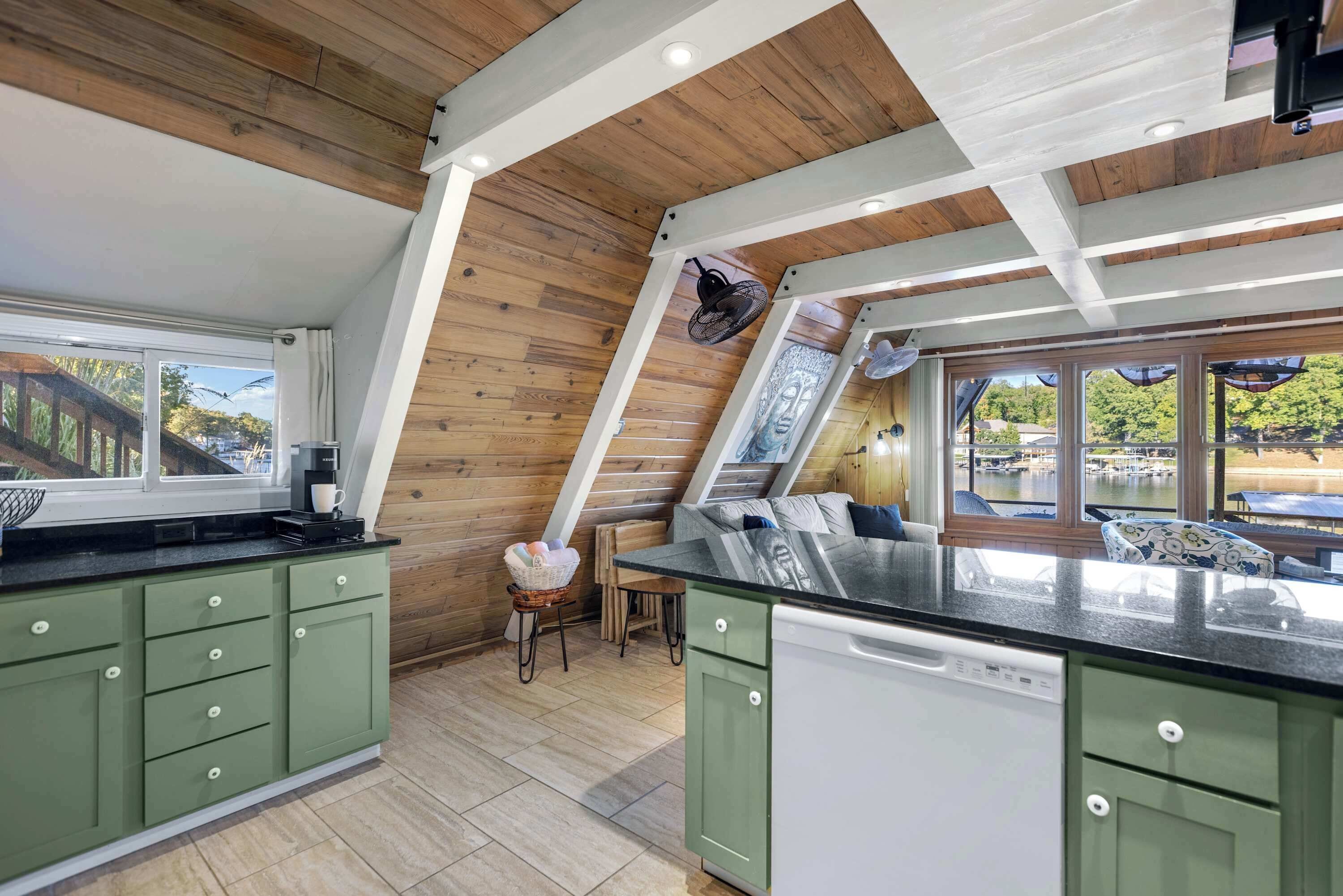 A modern kitchen with green cabinets, a black countertop, and a view of a lake.