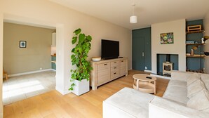 A modern living room with a sofa, a TV, a fireplace, and a large plant. - L'Oasis De Calmont - Piscine Privée (Calmont)