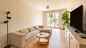 A modern living room with a beige sectional sofa, a round coffee table, a flat-screen TV, and a floor lamp. - L'Oasis De Calmont - Piscine Privée (Calmont)