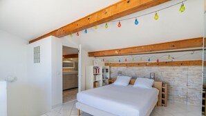 Un dormitorio con una cama grande, vigas de madera, una pared de piedra y una cocina al fondo.