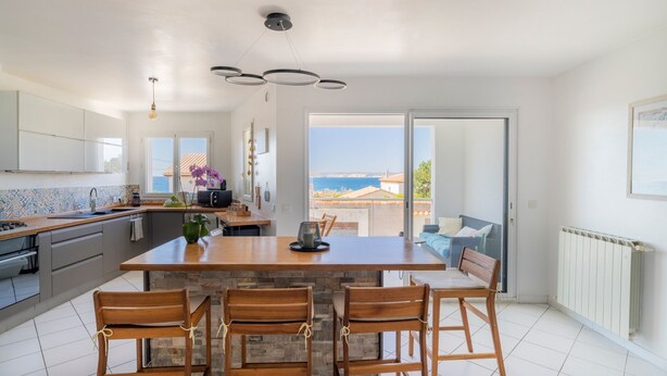 Una cocina moderna con una isla central, sillas de madera y vista al mar a través de un ventanal.
