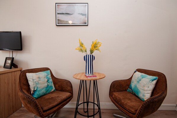 Two brown armchairs with teal pillows, a small round table with a vase of yellow flowers, and a framed picture on the wall.