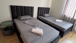 A hotel room with two beds, grey bedding, a small round table, and an air conditioning unit. - Velvet Vouge Hostel (Yerevan)