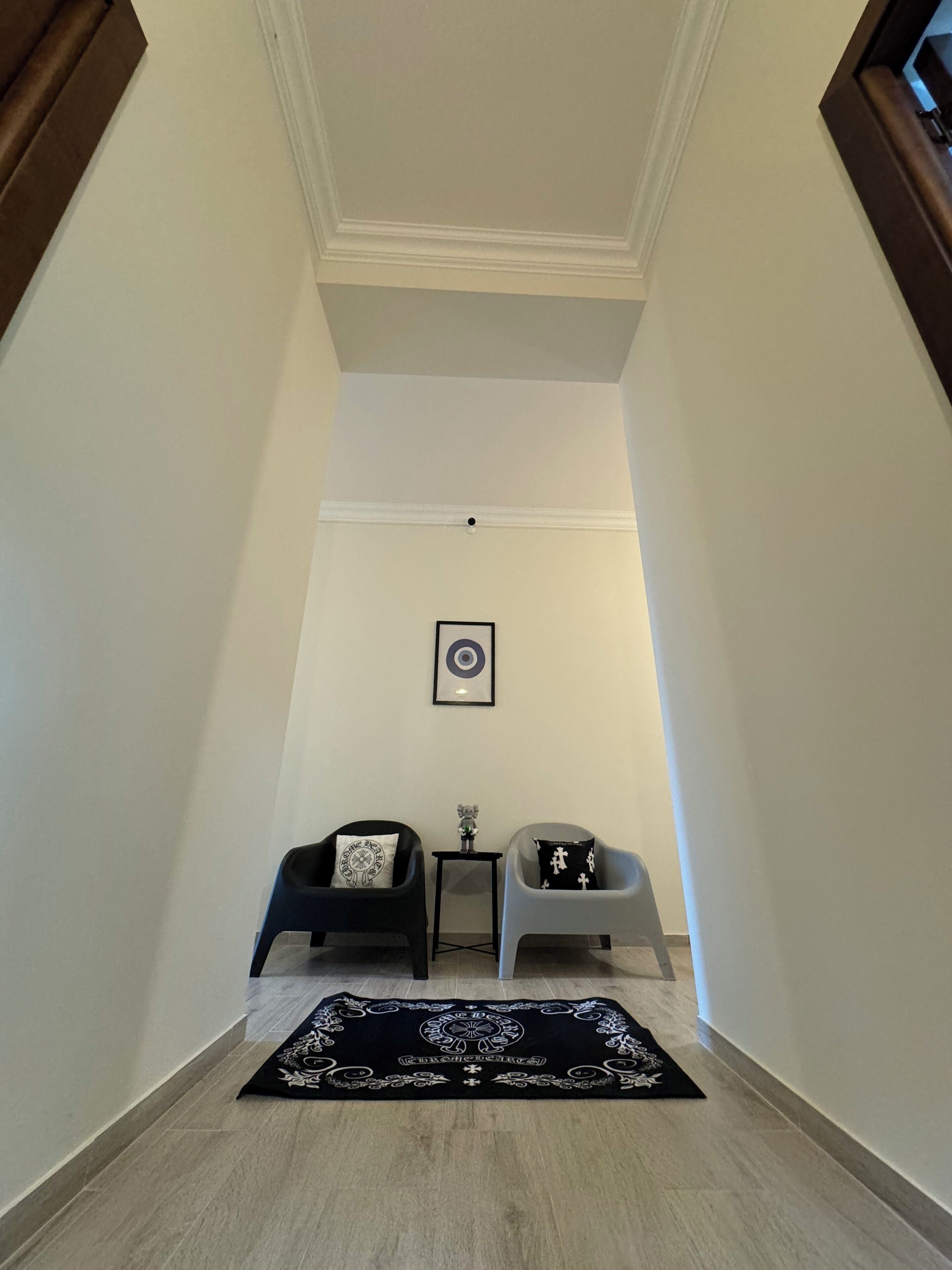 Un couloir étroit avec deux chaises et une petite table, un tableau encadré au mur et un tapis à motifs sur le sol.