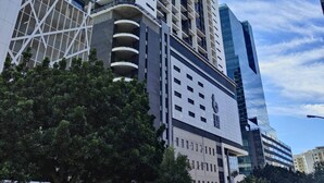 Un edificio moderno de gran altura con varios pisos y balcones, rodeado de otros edificios altos y árboles.