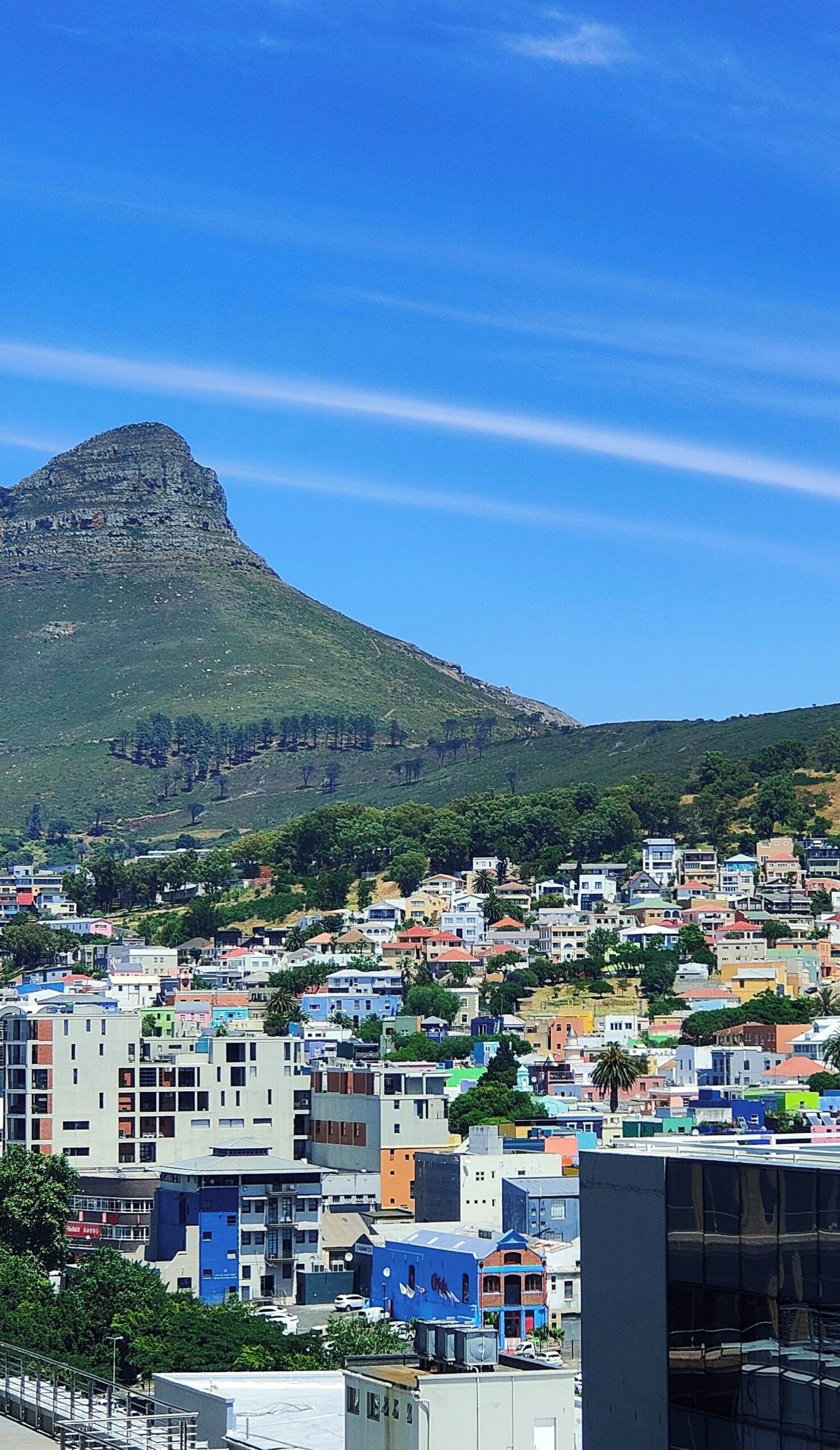 A coastal cityscape with a prominent mountain in the background, colorful buildings, and a clear blue sky.