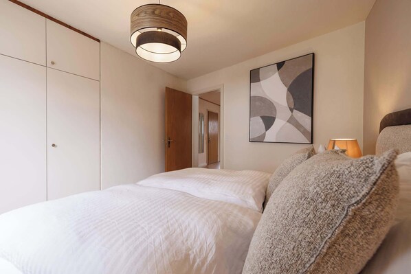 A bedroom with a bed, a hanging light fixture, a door, and a wall-mounted abstract painting.
