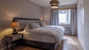 Une chambre moderne avec un grand lit, une table de chevet avec une lampe, une fenêtre avec des rideaux et un radiateur.