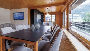 Un intérieur moderne avec un plafond en bois, un coin repas comprenant une table et des chaises, un espace cuisine et de grandes fenêtres offrant une vue sur l’extérieur.