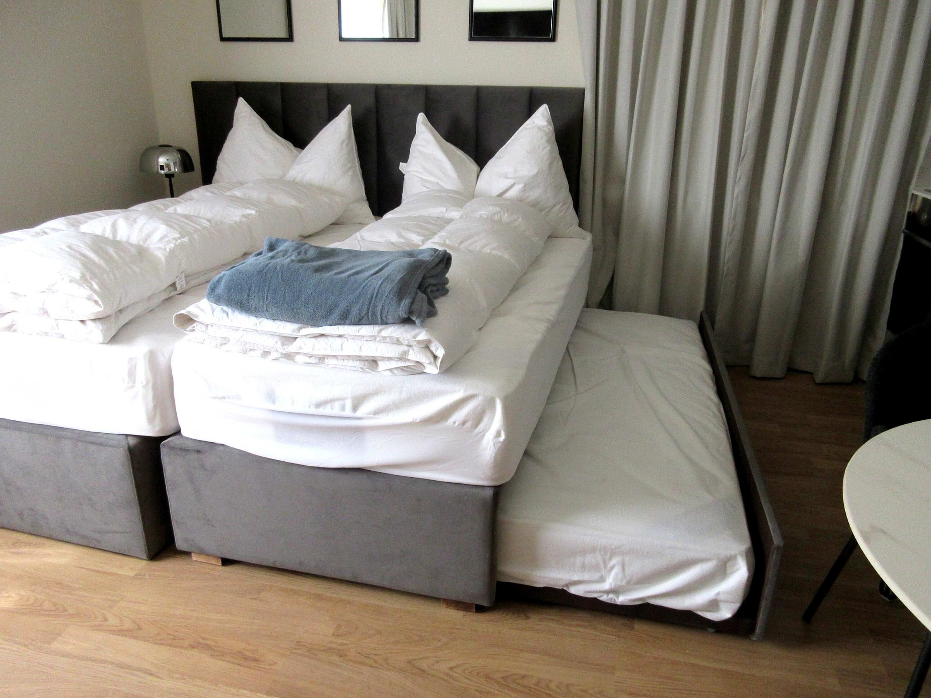 A neatly made bed with white linens and pillows, a gray blanket, and a bedside lamp.