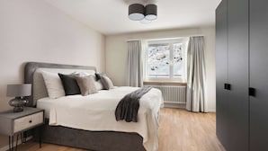 Ein modernes Schlafzimmer mit Bett, Nachttisch, Lampe und einem Fenster mit Vorhängen.