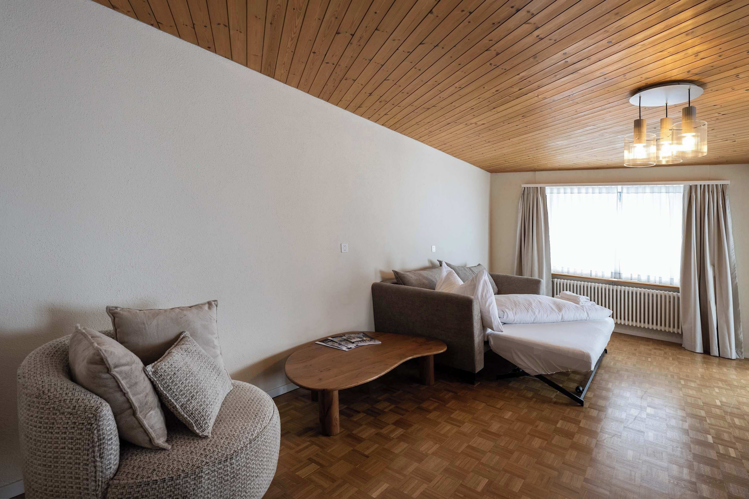 En moderne stue med træloft, en sofa, en lænestol og et lille bord.