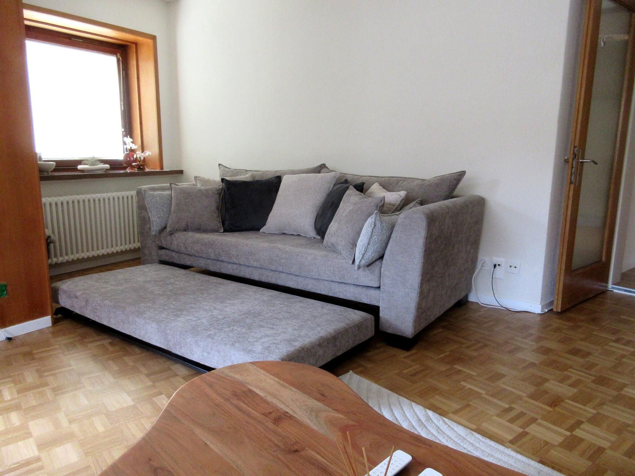 Un salon moderne avec un canapé gris, une table basse en bois et une fenêtre équipée de stores.