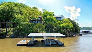 A dock with a covered seating area, a boat, and a house surrounded by trees. - Sunset Escape - Fit For 8 (Gravois Mills)