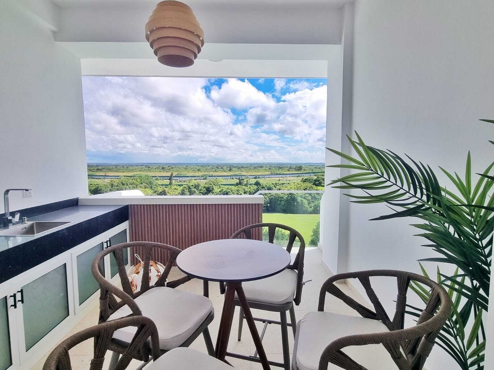 A balcony with a view of a green landscape, a round table with chairs, and a hanging light fixture.