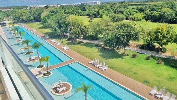Ein langer Swimmingpool mit Liegestühlen und Palmen, umgeben von üppiger Vegetation und einem entfernten Gebäude.