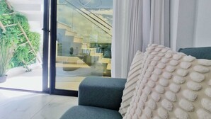 Ein modernes Wohnzimmer mit einem grauen Sofa, einem weißen Kissen mit Struktur und Blick auf eine Treppe, die zu einem Balkon führt.
