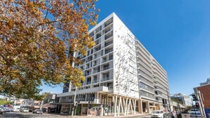 Un edificio moderno de varios pisos con una fachada distintiva, ventanas amplias y una entrada a nivel de calle con fachada de vidrio.