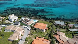 Luchtbeeld van een kustgebied met woningen, een zwembad en helder turquoise water.