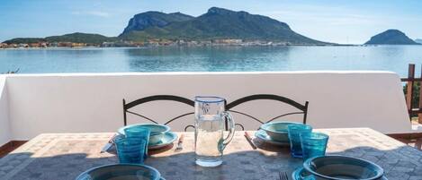 A table set for two with blue glassware and plates, overlooking a body of water and mountains.
