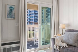Une pièce dotée d’une porte-fenêtre coulissante donnant sur un balcon, d’un climatiseur blanc, d’un canapé gris avec un plaid blanc et d’un tableau encadré accroché au mur.