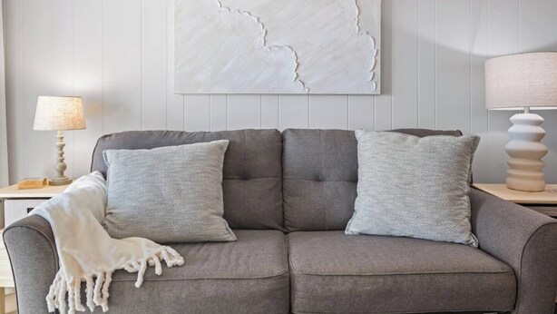 A grey sofa with two grey cushions and a white throw blanket.