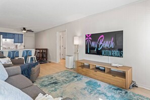 A modern living room with a flat-screen TV, a sofa, a coffee table, and a dining area with chairs.