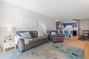 A modern living room with a sofa, ottoman, and a dining area with a table and chairs. - Ocean View Shore Drive Bliss- Pool- Grills- Slps 6 (Myrtle Beach)