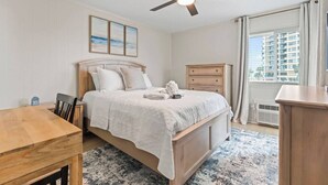 A bedroom with a bed, a desk, a chair, a dresser, and a ceiling fan.