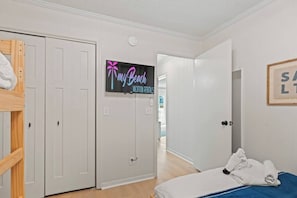 A hotel room with a bunk bed, a flat-screen TV, a framed picture, and a door leading to a hallway. - Ocean View Shore Drive Bliss- Pool- Grills- Slps 6 (Myrtle Beach)
