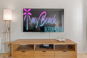 Un téléviseur à écran plat fixé au mur, avec une pancarte indiquant : « Mes locations de vacances à la plage ».