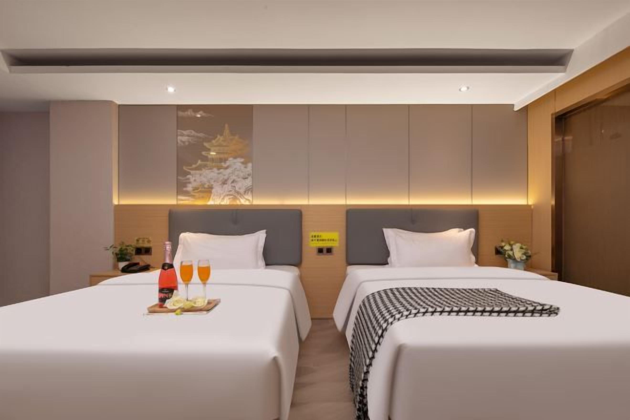 Habitación de hotel con dos camas, una mesita de noche, una obra de arte colgada en la pared y una pequeña mesa con una botella y vasos.
