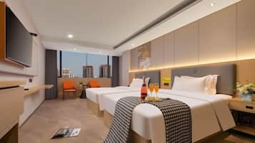 A hotel room with two beds, a TV, a desk, and a view of buildings.