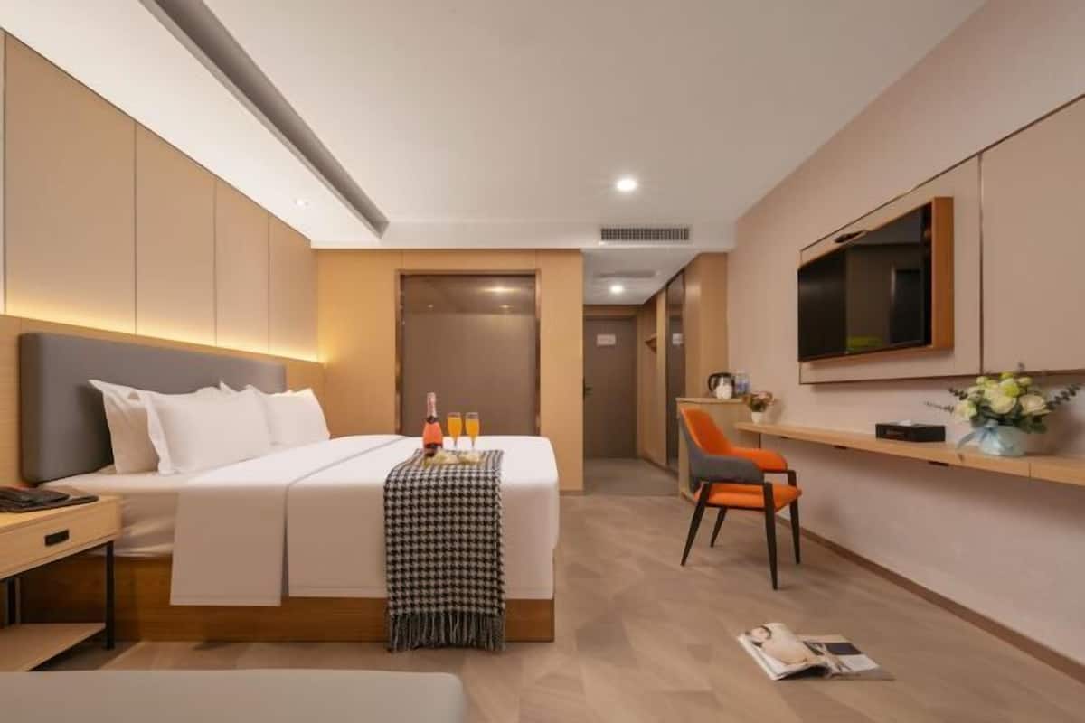 Moderni hotellihuone, jossa on sänky, yöpöytä, televisio ja pieni työpöytä.