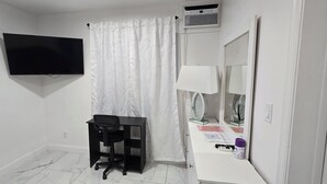 A small, clean room with a desk, chair, mirror, and a television mounted on the wall. - Charming studio with AC and WiFi in brilliant Tampa (Tampa)