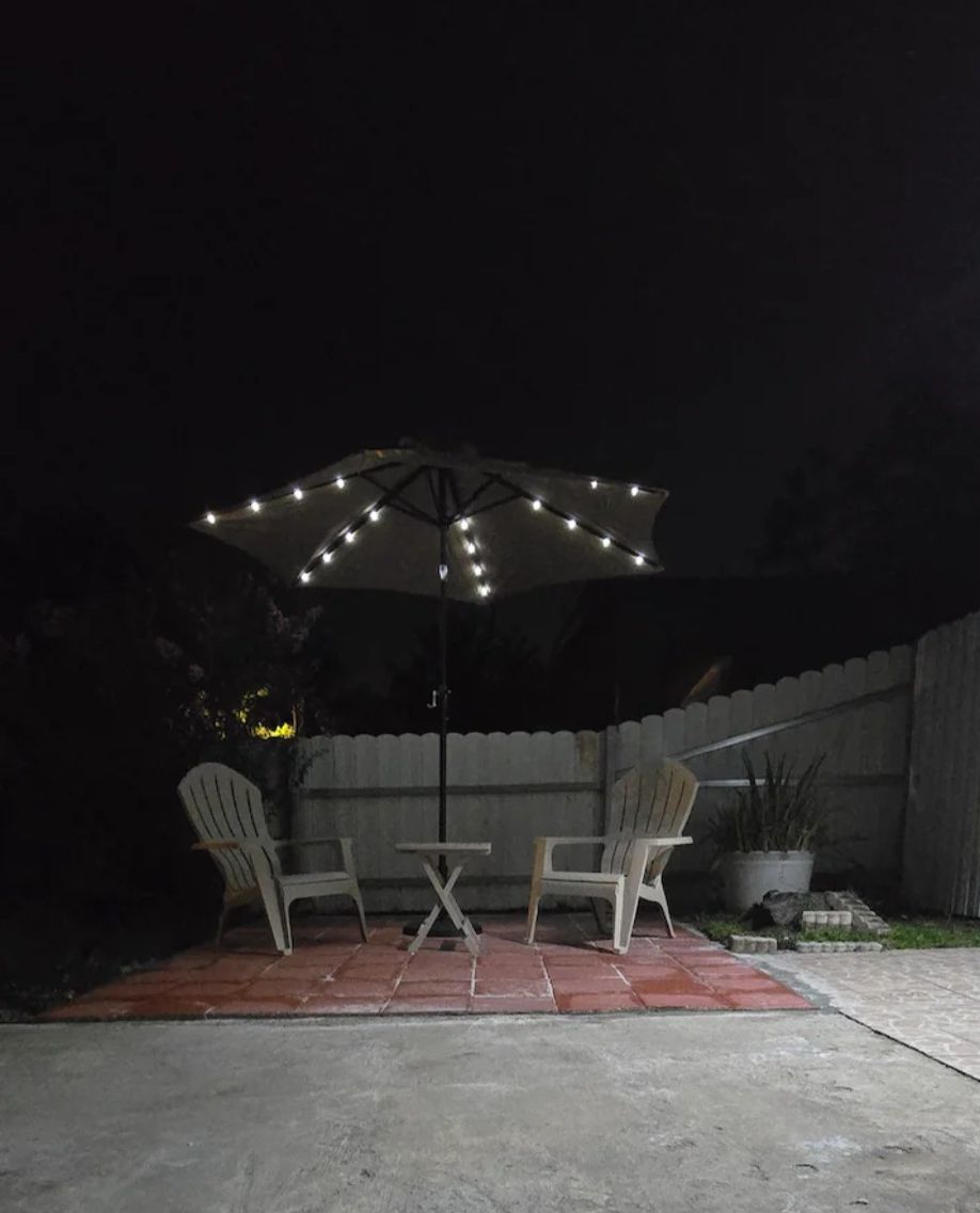Un patio al aire libre con dos sillas y una mesa bajo un paraguas iluminado con luces.