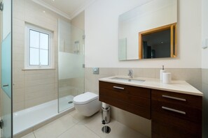 Ein modernes Badezimmer mit Duschkabine aus Glas, Toilette, Waschbecken mit Spiegel und Mülleimer.