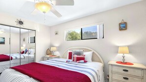 Un dormitorio con cama, mesitas de noche, espejo, ventana y ventilador de techo.