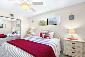 Quarto com cama, mesas de cabeceira, espelho, janela e ventilador de teto.
