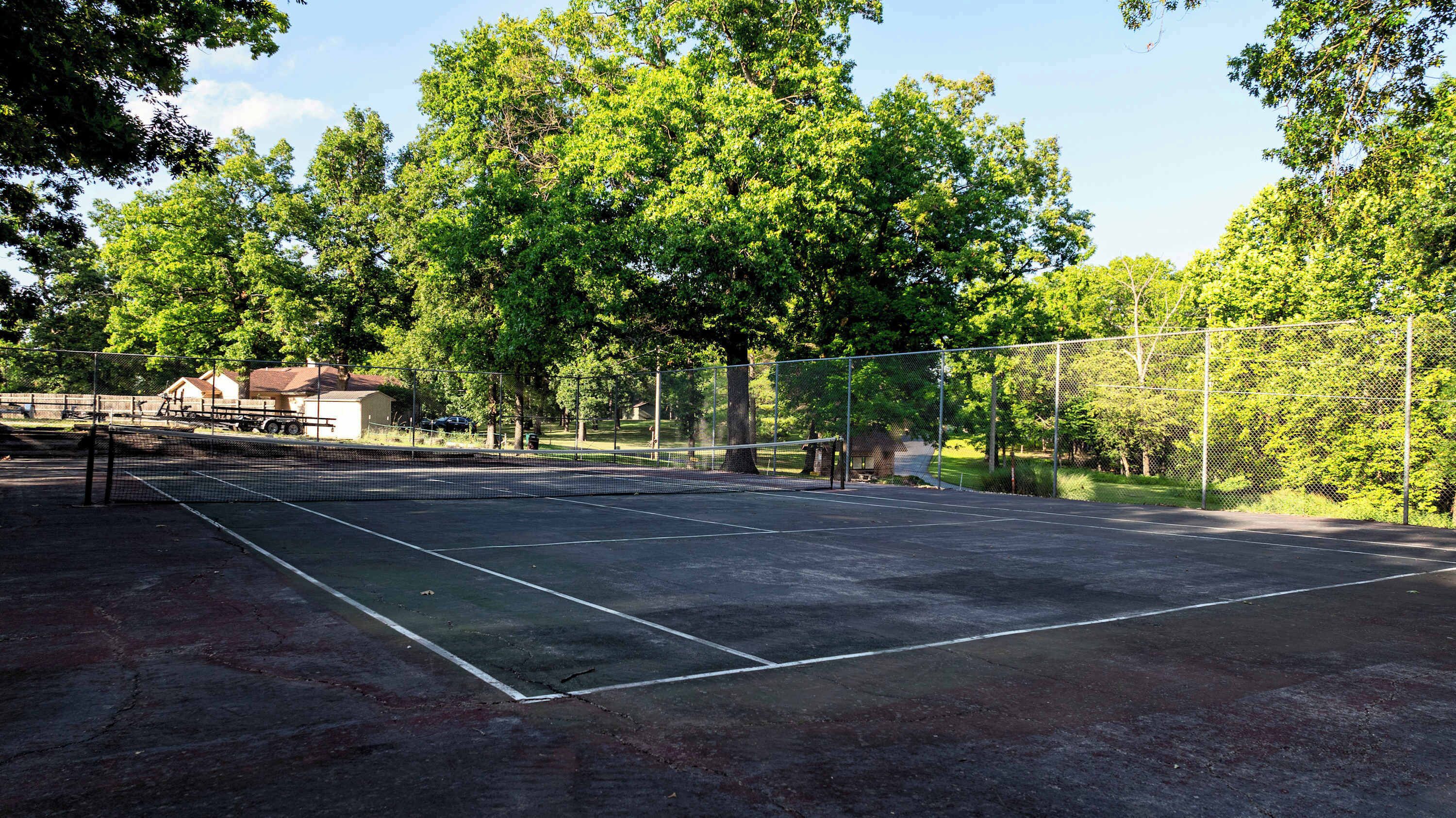 An outdoor tennis court surrounded by trees and a fence.