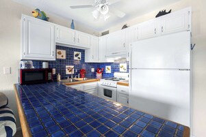 Uma cozinha com armários brancos, painel de azulejos azuis, micro-ondas, fogão e geladeira.