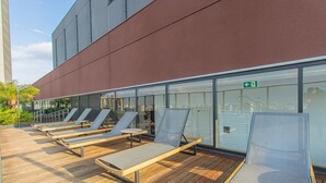 A rooftop lounge area with sun loungers and a glass wall overlooking the city. - Cozy Near Allianz Parque Sp-p1609a (São Paulo)