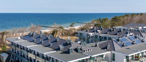 Un edificio moderno de varios pisos con paneles solares en el techo, situado cerca de una playa y con vistas despejadas al océano.